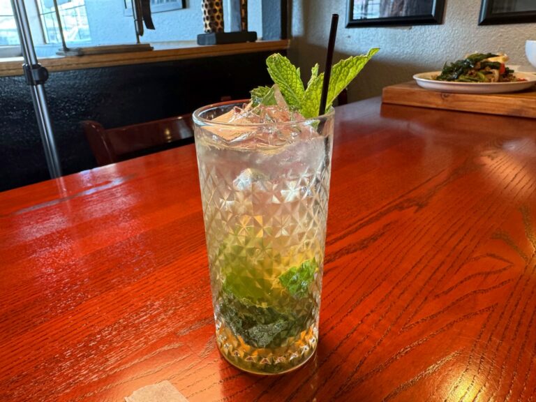 A mint and citrus cocktail on a dining table in the Nakhon Luang dining room, with a plate of food behind it