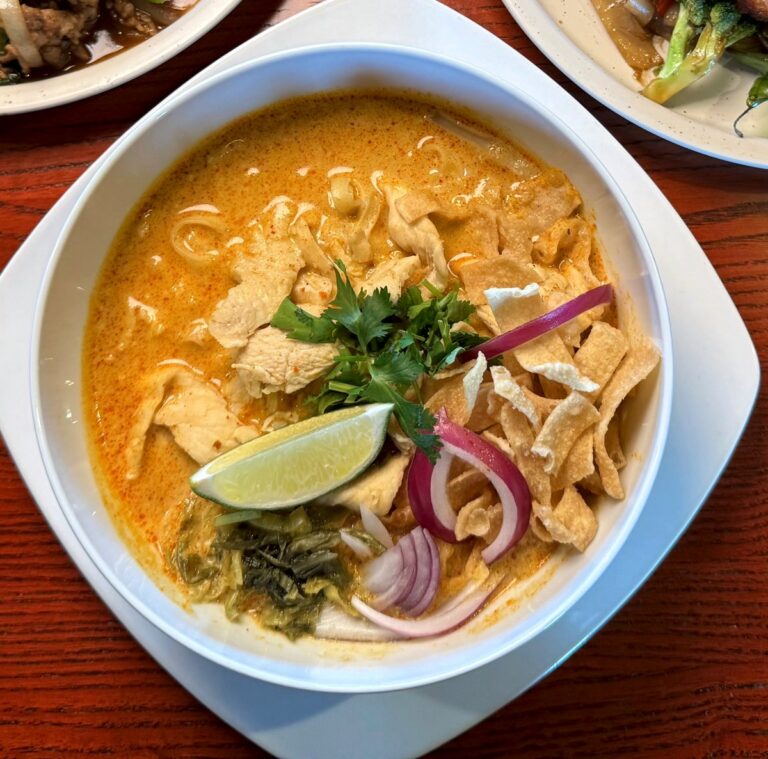 Khao soi noodle soup topped with crispy noodles, red onion, cilantro and lime