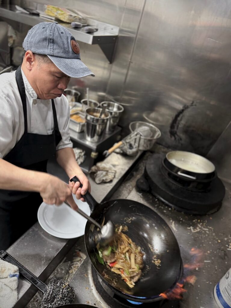 Chef Toui stir frying noodles in a wok over an open flame in the Nakhon Luang kitchen